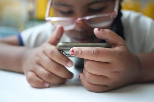 Young girl with glasses engages with a smartphone closely.
