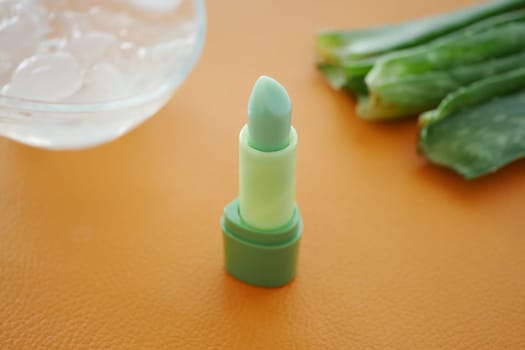 Fresh green lip balm beside aloe vera leaves and ice cubes.