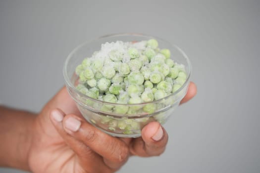 A hand holds a clear bowl of vibrant green peas.