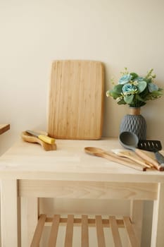 A tidy kitchen counter with a wooden board, utensils, and flowers.