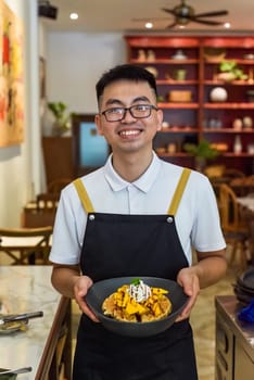Vietnamese man chef in uniform holding fresh baked belgian waffles with cream and sliced mango fruit in cafe