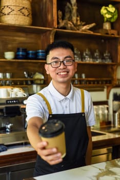 Vietnamese smiling waiter holding paper cups with coffee in a cafe