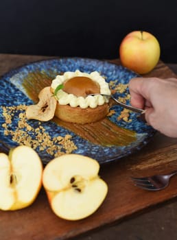 Piece of apple tart in a spoon with fresh apples on wooden table