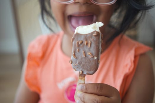 Young girl with glasses happily holds chocolate ice cream treat, smiling wide.