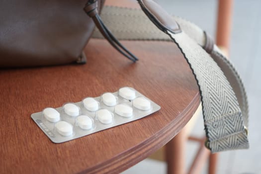 White pills are arranged neatly on a wooden table beside a handbag strap.