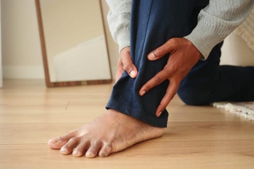 Individual holds their ankle in discomfort while kneeling at home.