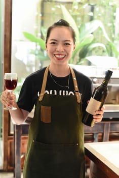 Happy vietnamese waitress smiling and holding a bottle of homemade plum wine and glass of wine