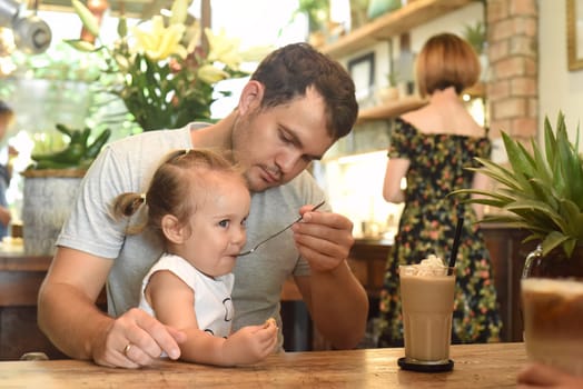 Father and daughter eating cream from frappe in a cafe
