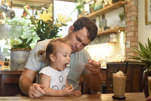 Father and daughter eating cream from frappe in a cafe