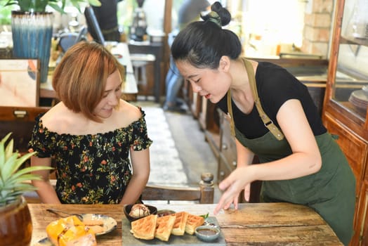 Vietnamese waitress serve Belgium waffles to a Caucasian woman
