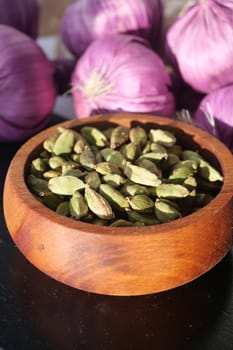 Cardamom seeds fill a bowl, surrounded by purple onions.