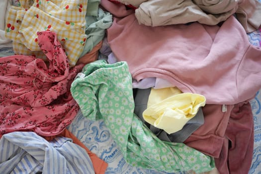 Colorful wrinkled clothes scattered on a bed show it's laundry day.