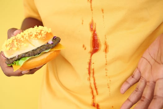 A person spills ketchup on their shirt while holding a burger.