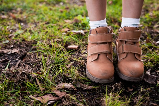 Childs brown boots on grass with autumn leaves.