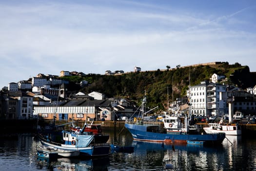 Village of Luarca, Spain. January 22, 2025. Fishing boats in scenic coastal town harbor with hillside houses.