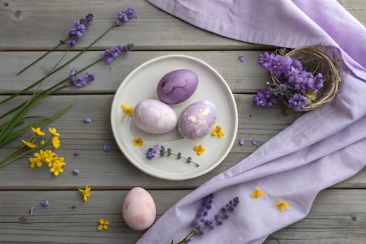 A serene spring-themed flat lay featuring pastel-colored Easter eggs, lavender flowers, and yellow blossoms, perfect for Easter decoration or seasonal celebrations. Easter concept.