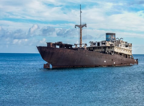 A rusting shipwreck in the blue ocean symbolizes abandonment and mystery on a bright, cloudy day.