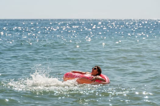 A person floats on a pink inflatable ring in the ocean, the water is sparkling with sunlight.