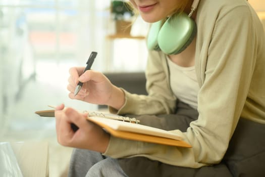 Smiling young woman sitting on a couch and writing in her notebook.