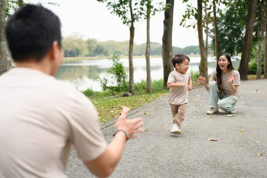 Happy little boy running towards his parents on a park path.