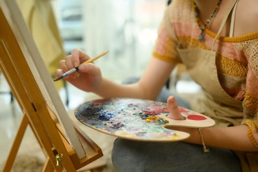 Close up of artist hand holding holding a palette and painting on a canvas.