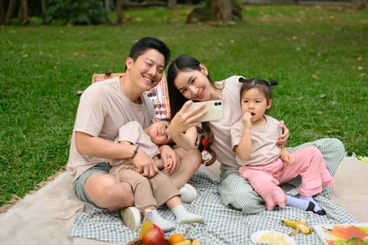 Cheerful family taking a selfie with mobile phone during their outdoor picnic.