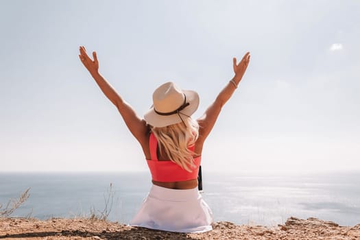 A woman wearing a pink top and a straw hat is sitting on a beach, looking out at the ocean. She is smiling and she is enjoying the view