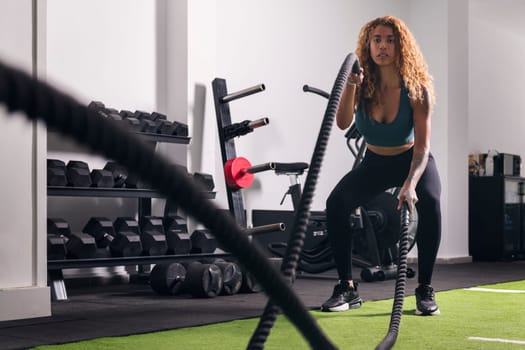 muscular sportswoman doing exercise with rope during functional workout at gym, concept of fitness and active lifestyle
