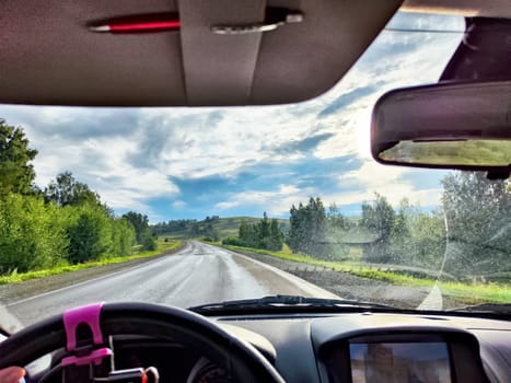 view through car windshield of nature landscape with green field, mountains, white clouds. Hand of woman on steering wheel. Female traveler
