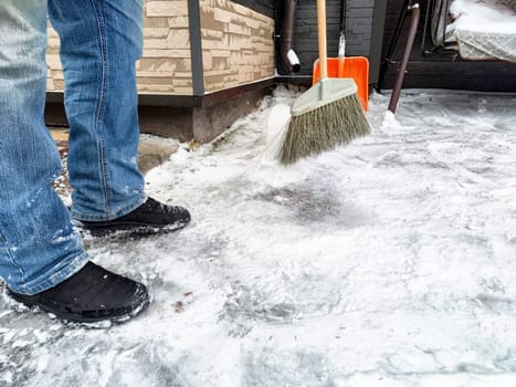 Snow is being cleared from a residential walkway as a person uses a broom to remove ice and snow from the pavement during winter.