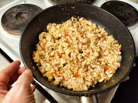 Fried rice is being stirred in a skillet on a stovetop, showcasing chicken pieces and colorful vegetables being prepared.