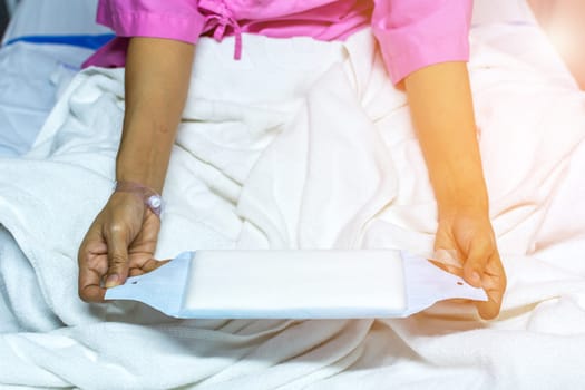 Patient asian woman with adhesive plaster on hand using sanitary napkin for menstruation on patient bed in the hospital