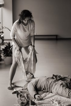 A therapist gently drapes a colorful scarf over a patient lying on a comfortable mat in a calm studio. The serene space is adorned with plants, creating a peaceful environment for healing and relaxation.