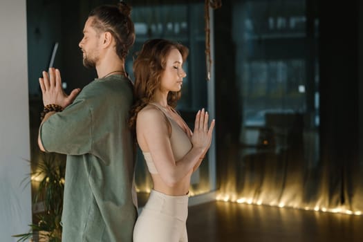 Two practitioners engage in a meditative exercise, seated back to back in a tranquil indoor environment. The soft lighting creates a calming atmosphere, enhancing their focus on breathing and mindfulness during the session.