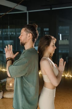 Two practitioners engage in a meditative exercise, seated back to back in a tranquil indoor environment. The soft lighting creates a calming atmosphere, enhancing their focus on breathing and mindfulness during the session.