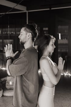 Two practitioners engage in a meditative exercise, seated back to back in a tranquil indoor environment. The soft lighting creates a calming atmosphere, enhancing their focus on breathing and mindfulness during the session.