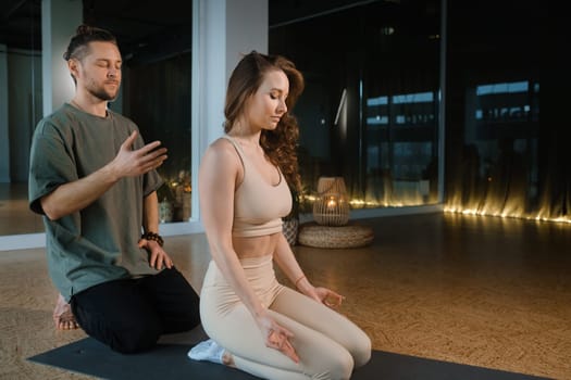Two individuals engage in a calming yoga and meditation practice inside a serene studio. The dimly lit space features soft lighting and a peaceful atmosphere, enhancing their focus and mindfulness.