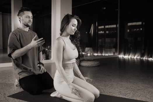 Two individuals engage in a calming yoga and meditation practice inside a serene studio. The dimly lit space features soft lighting and a peaceful atmosphere, enhancing their focus and mindfulness.