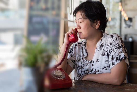 Asian women 40s white skin in black and white shirt unhappy and dismal between waiting something or talking phone call in a coffee shop cafe with a red telephone vintage style
