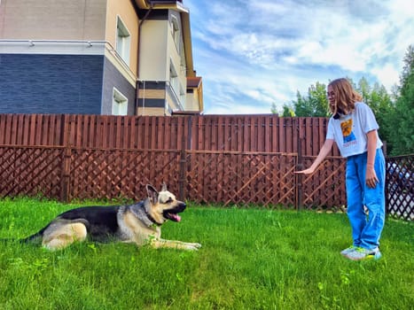 A child practices commands with a German Shepherd in a green backyard during a sunny day, focused on learning and bonding.