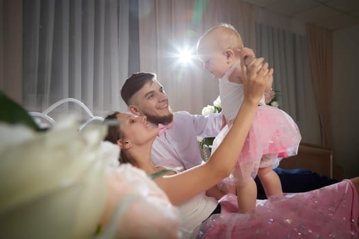 A couple enjoys a tender moment while their baby girl plays with a toy in a warm, inviting space filled with soft lighting on bed in beautiful room
