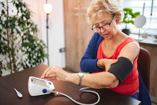 Senior lady checks blood pressure with a monitor in a cozy setting.