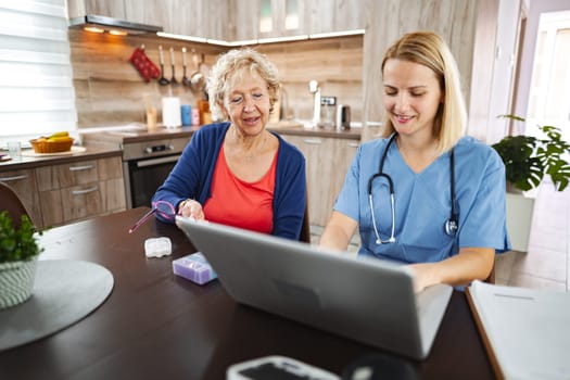 Nurse and elderly woman discuss health in a modern kitchen.