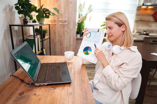 Woman analyzes colorful charts while working on her laptop in a bright space.