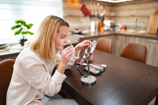 A woman carefully enhances her features at a stylish kitchen table.