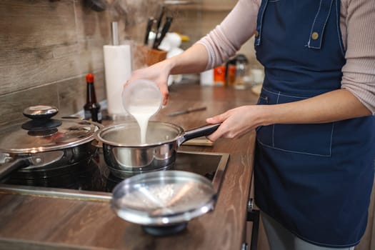 A cook adds fresh milk to a pot, creating a rich mixture in the kitchen.