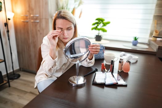 Elegant woman focuses on her makeup routine at home, showcasing artistry.