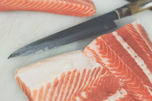 Asian chef slice salmon by knife on boad for japanese food delicacy consisting sashimi salmon of very fresh raw salmon fish sliced into thin pieces serving with radish sliced in japanese restaurant