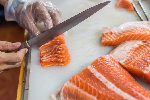 Asian chef slice salmon by knife on boad for japanese food delicacy consisting sashimi salmon of very fresh raw salmon fish sliced into thin pieces serving with radish sliced in japanese restaurant