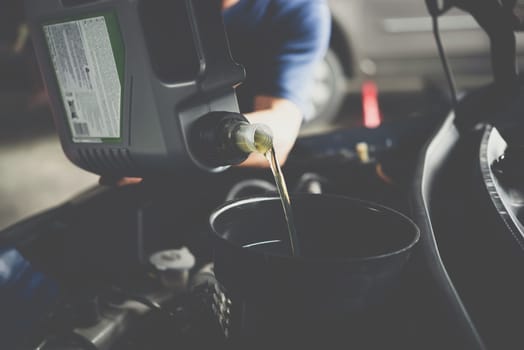 Car mechanic or serviceman fills a fresh lubricant engine oil at car garage for repair or maintenance a car